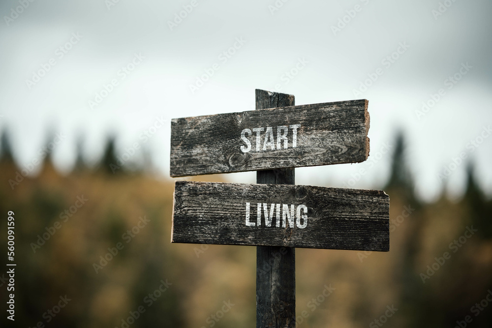 vintage and rustic wooden signpost with the weathered text quote start living, outdoors in nature. blurred out forest fall colors in the background.