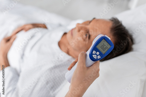 Doctor holding pyrometer near blurred elderly patient in clinic. photo