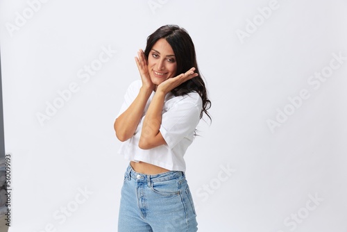Woman in white t-shirt on white background brunette hands up gestures and signals poses in jeans emotion, lifestyle smiles, copy space
