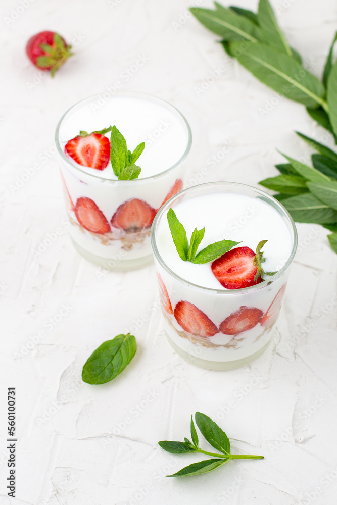 White yogurt with fresh strawberries granola and mint in two glasses on a white background. White yogurt with fresh strawberries granola and mint in two glasses on a white background.