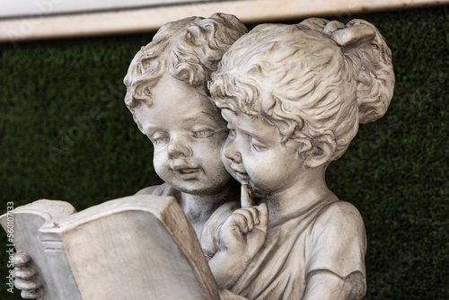girls reading, plaster figure Old white statue of children reading a book.