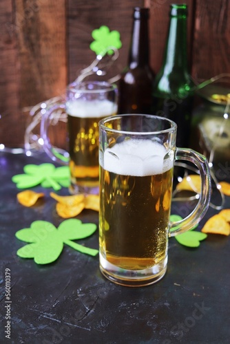 Patrick's Day, foamy beer in glass mugs and a bottle, chips and cookies, green shamrocks and gold coins, on a wooden background, party, St. Patrick's Day celebration