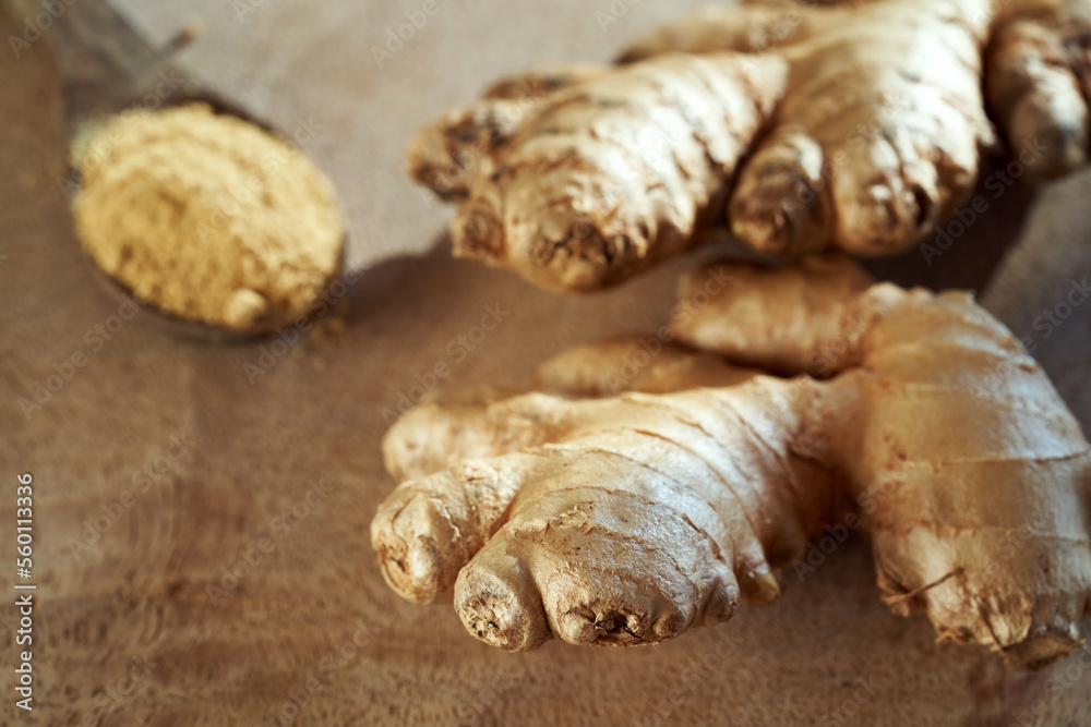 Fresh whole ginger root, with ginger powder in the background