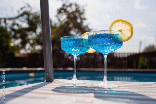 Foto A glass of delicious blue cocktail Blue Lagoon and yellow lemons on the background of the pool