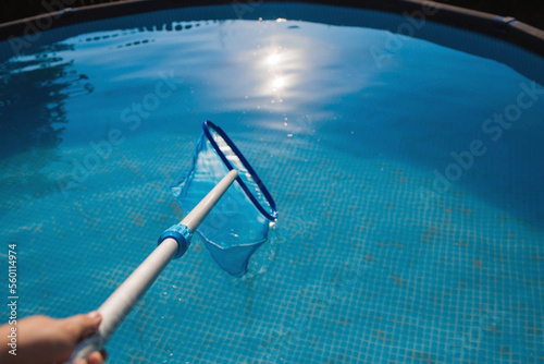 Abstract blur and defocused background. Cleaning of a swimming pool with a metal frame with a mesh from dirt. Pool cleaner during operation. Solar banner.The concept of summer holidays.