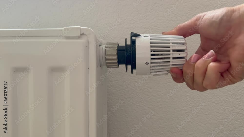 Hand of woman adjusting thermostat valve of heating radiator in a room Hand of woman adjusting thermostat valve of heating radiator in a room