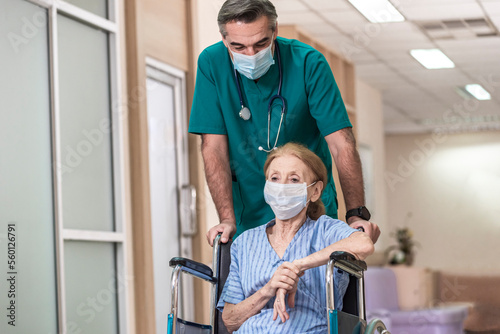 Assistance Doctor staff help senior patient wear protective face mask and sit on wheelchair after recovering from cancer treatment with cremo therapy in the hospital photo