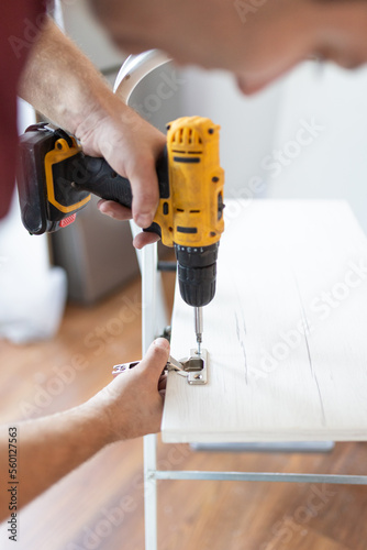 Close up man holding cordless screwdriver machine and screws lie for screwing a screw assembling furniture at home