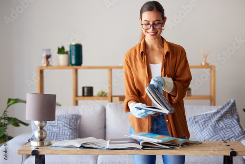 Cleaning, happy and woman with books in the living room, inspection and content with housework. Smile, check and cleaner spring cleaning a book for housekeeping and decluttering in lounge of a house photo