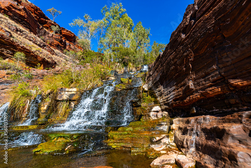 a panorama of fortescue falls in dales gorge in karijini national park in western australia; a waterfall in a lush red canyon in the desert with red sand and rocks