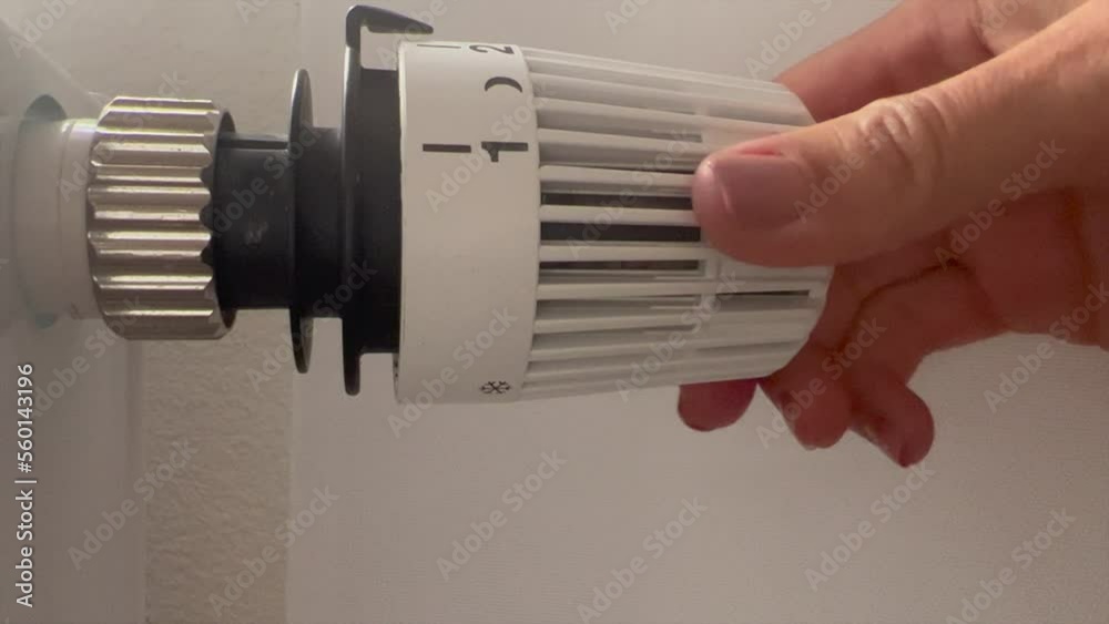 Hand of woman regulating the temperature in the house with a thermostat on the white radiator