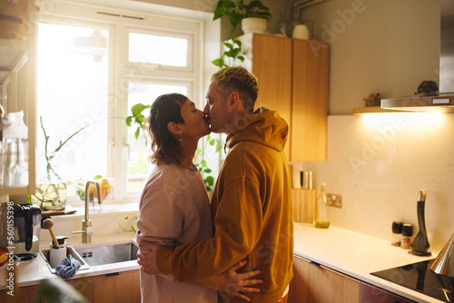 Young Happy Asian And Caucasian Same Sex Interracial Couple Kissing In Kitchen At Home In The Morning © Southworks