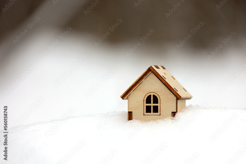 Wooden house model in a snow on winter forest background. Concept of country cottage, real estate in ecologically clean area