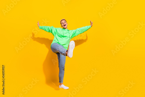Full body length photo of young overjoyed positive girl wear stylish hoodie with denim jeans new sneakers dance isolated on yellow color background
