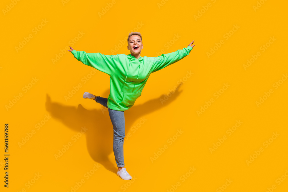 Full body size photo of young carefree relaxed woman flying bird hands wear green bright hoodie overjoyed isolated on yellow color background