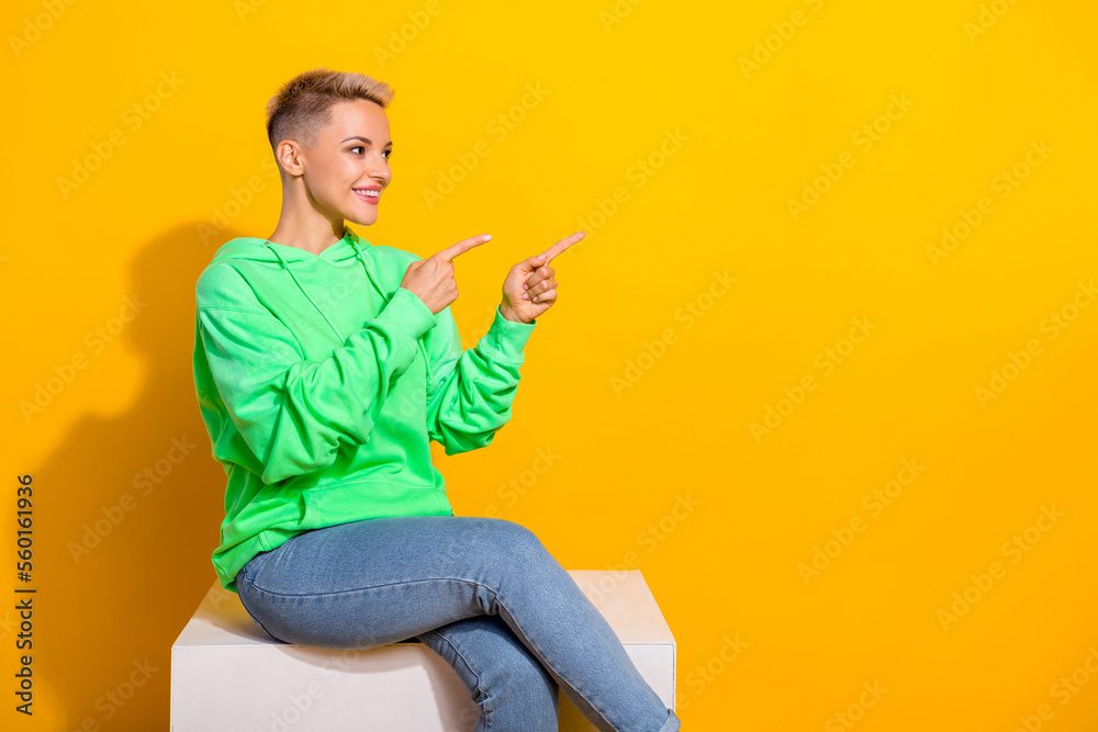 Profile photo of pretty positive girl sit podium look direct fingers empty space isolated on yellow color background Profile photo of pretty positive girl sit podium look direct fingers empty space isolated on yellow color background