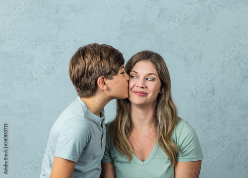 a tween son kissing his mom in her forties on the cheek with a green background