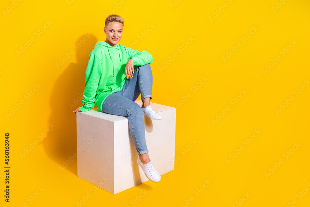 Full size photo of nice cheerful girl sit podium have good mood empty space ad isolated on yellow color background Full size photo of nice cheerful girl sit podium have good mood empty space ad isolated on yellow color background