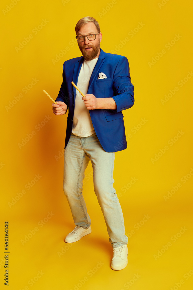 Joyful middle age man in bright blue jacket and trousers having fun isolated over yellow background. Concept of fashion, beauty, positive emotions Joyful middle age man in bright blue jacket and trousers having fun isolated over yellow background. Concept of fashion, beauty, positive emotions