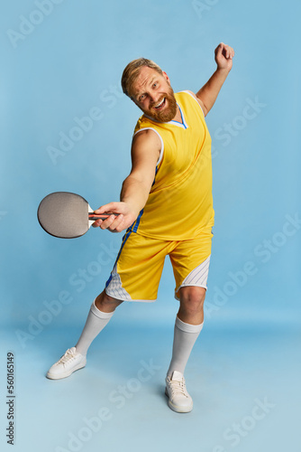 Excited happy man with beard wearing sportswear playing ping-pong isolated over blue background. Concept of active lifestyle, positive emotions, sport