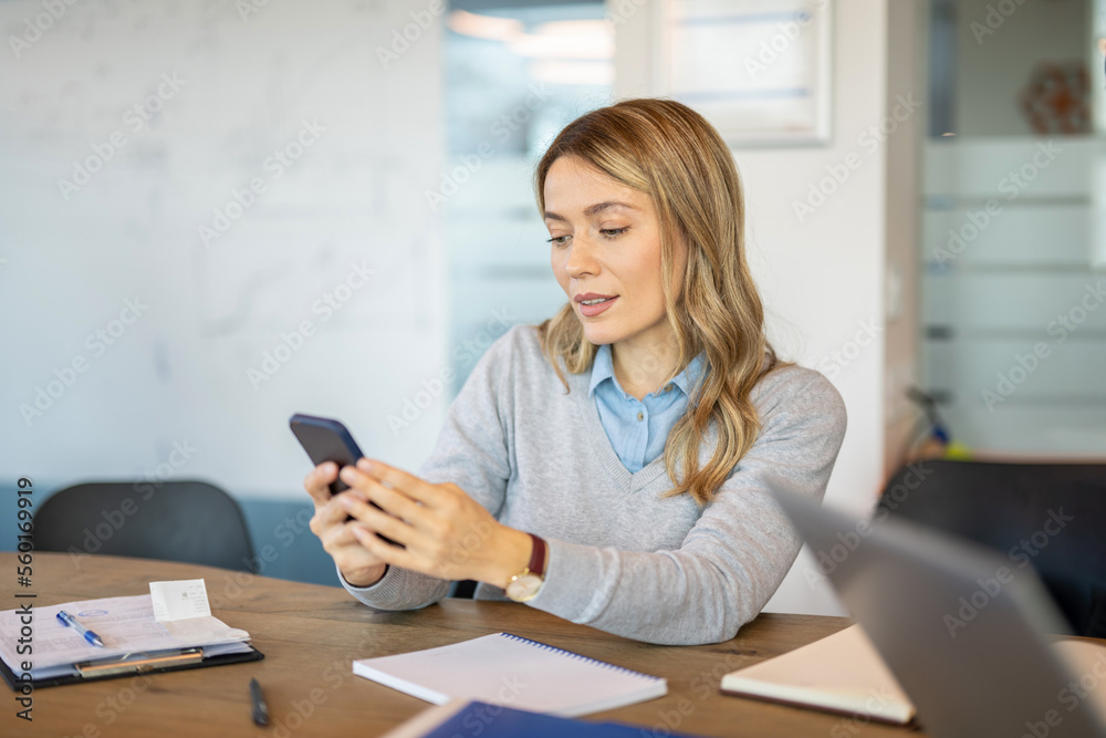 Businesswoman sitting at desk and text messaging while working at office. Businesswoman sitting at desk and text messaging while working at office.