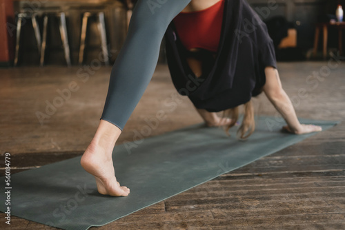 Young adult unrecognizable female yogi new teacher in three legged downward facing dog pose, workout yoga practice, barefoot wearing sportswear, green yoga mat on wooden floor, close-up photo photo