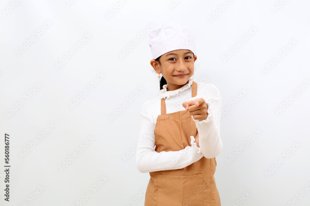 Happy little girl in chef uniform pointing at the camera. Isolated on white background Happy little girl in chef uniform pointing at the camera. Isolated on white background