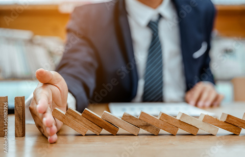 Strategy and successful intervention concept for business, businessman hand Stopping Falling wooden Dominoes effect from continuous toppled or risk.