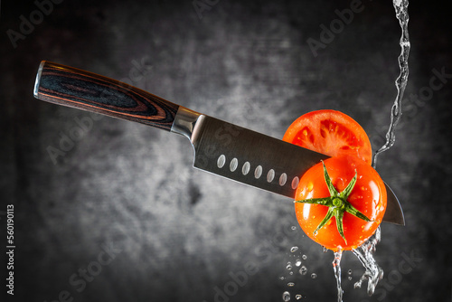 Messer schneidet durch frische Tomate und Wasser läuft runter.