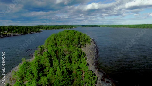 Low forward aerial flyover over a rocky island with pine trees. Islet in the middle of the lake with water waves, cloudy blue sky. Vänern lake in Värmland Sweden photo