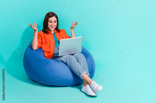 Full length photo of impressed girl dressed orange shirt bean bag talking device empty space isolated turquoise color background