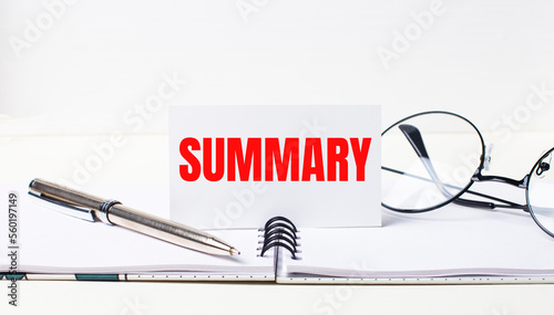 Close-up of a white card with the text SUMMARY, a stylish pen and glasses on a desktop.