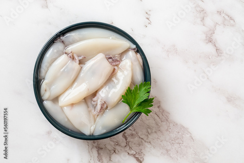 Raw squid fillet in a bowl over marble background. Small calamary tubes prepared for cooking. Fresh squid molluscs ingredient for low calorie healthy diet. Seafood concept.