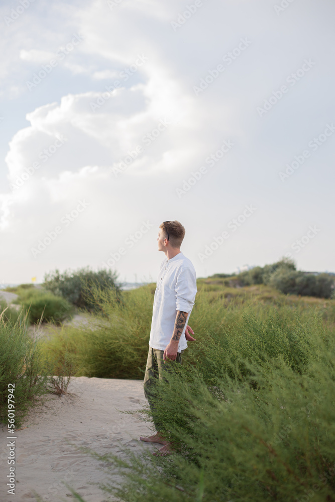 a man in a white shirt stands on the sand dunes looks up to the sky, looks thoughtfully up