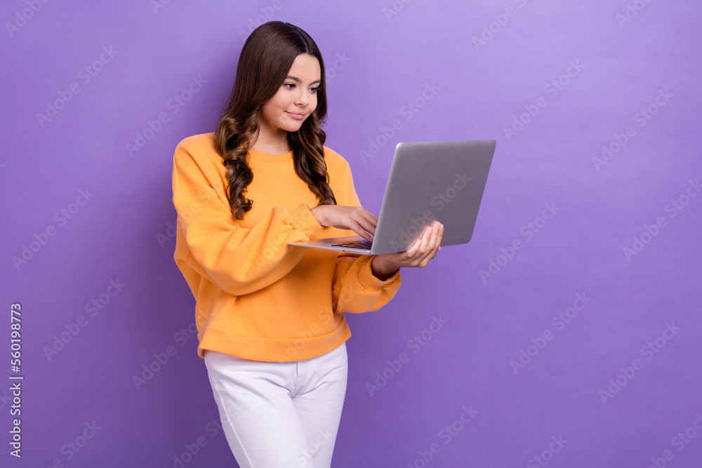 Photo of pretty sweet girl dressed orange sweatshirt typing modern device empty space isolated purple color background Photo of pretty sweet girl dressed orange sweatshirt typing modern device empty space isolated purple color background