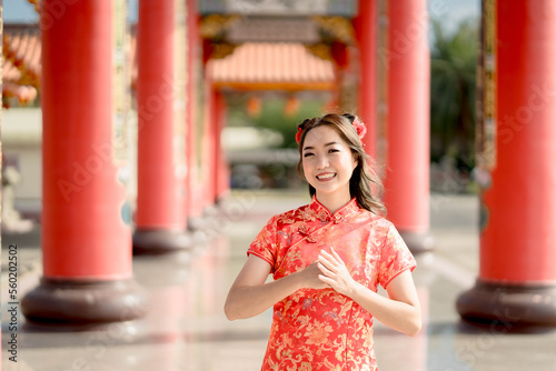 Asian woman wearing traditional cheongsam qipao dress with gesture of congratulation in Chinese Buddhist temple. Emotion smile. Chainese new year concept. Emotion Smile