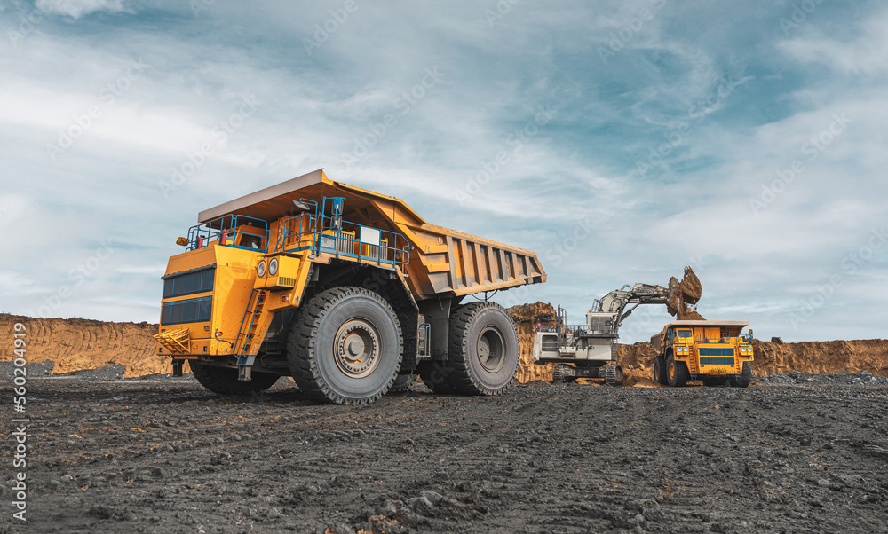 Large quarry dump truck. Big yellow mining truck at work site. Loading coal into body truck. Production useful minerals. Mining truck mining machinery to transport coal from open-pit production Large quarry dump truck. Big yellow mining truck at work site. Loading coal into body truck. Production useful minerals. Mining truck mining machinery to transport coal from open-pit production