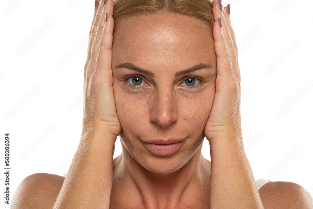 Middle aged blond woman tightens her face with her hands on a white background Middle aged blond woman tightens her face with her hands on a white background