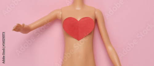 The naked body of a doll with a heart on a pink background. Love concept