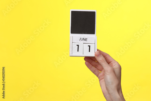 Woman's hand holds wooden calendar with date june 11 on a yellow background