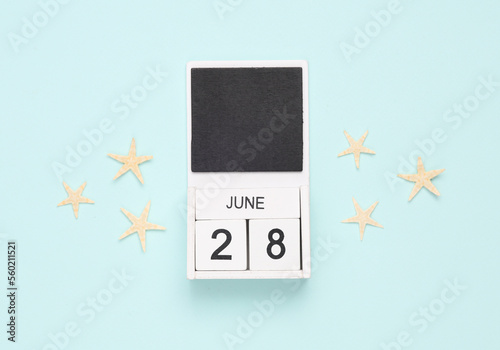 White wooden calendar with the date june 28 and sea stars on a blue background. Summer time. Top view photo