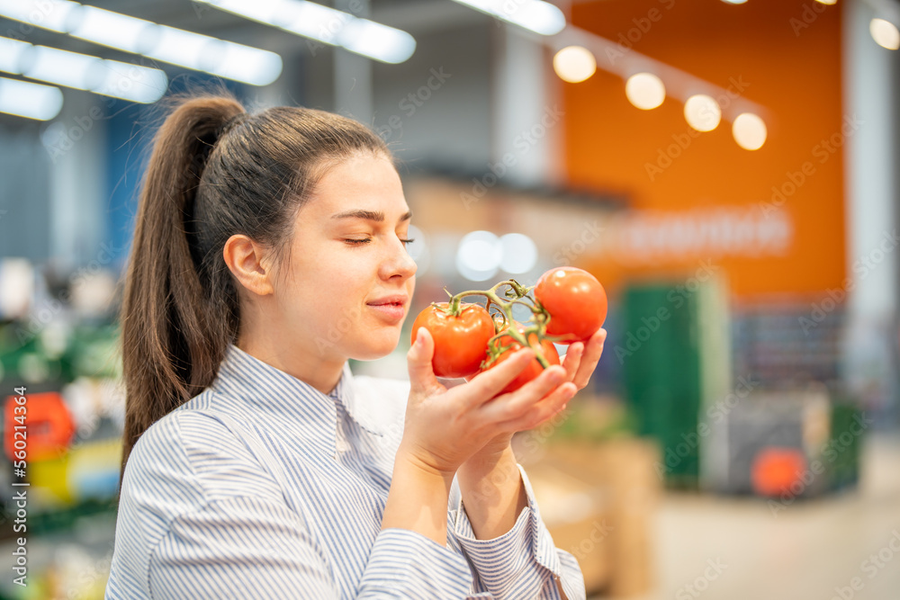 Young woman holding and smelling fresh organic tomatoes with the eyes closed at the vegetable section in a supermarket. Healthy nutritional choice. Woman enjoying the smell of organic raw vegetables Young woman holding and smelling fresh organic tomatoes with the eyes closed at the vegetable section in a supermarket. Healthy nutritional choice. Woman enjoying the smell of organic raw vegetables