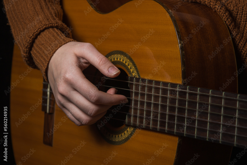 Fototapeta premium Female hands play an acoustic guitar on a black background. To play guitar