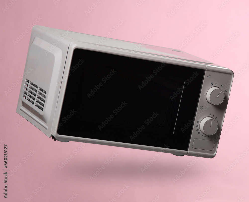 Fototapeta premium Wireless microwave oven levitating on pink background with shadow