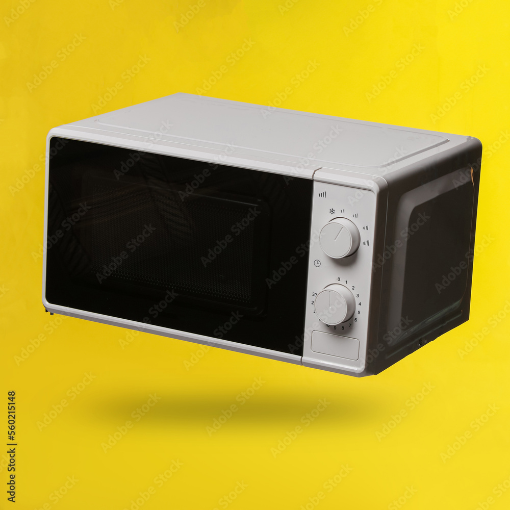 Fototapeta premium Wireless modern microwave oven levitating on yellow background with shadow