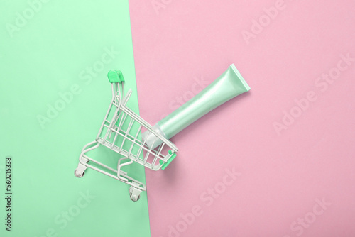 Supermarket trolley with tube of foundation on green pink pastel background