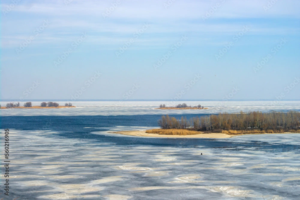 Ice drift on Dnieper river in Cherkasy city, Ukraine at sunny spring day. Picturesque islands. Lonely figure of fisherman on the ice