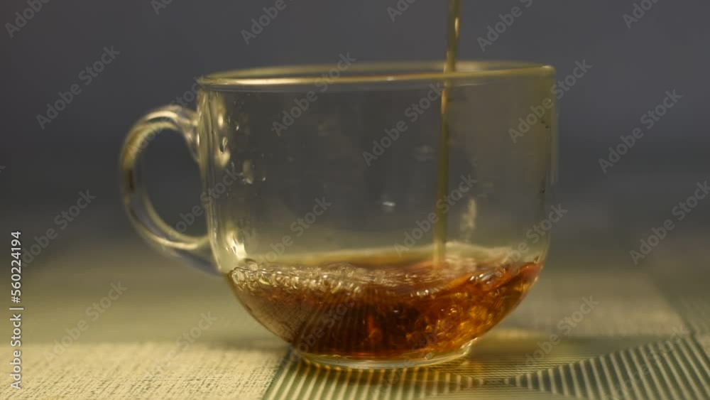Hot tea is poured into a transparent glass goblet, gradually filling the container. Hot tea is poured into a transparent glass goblet, gradually filling the container.