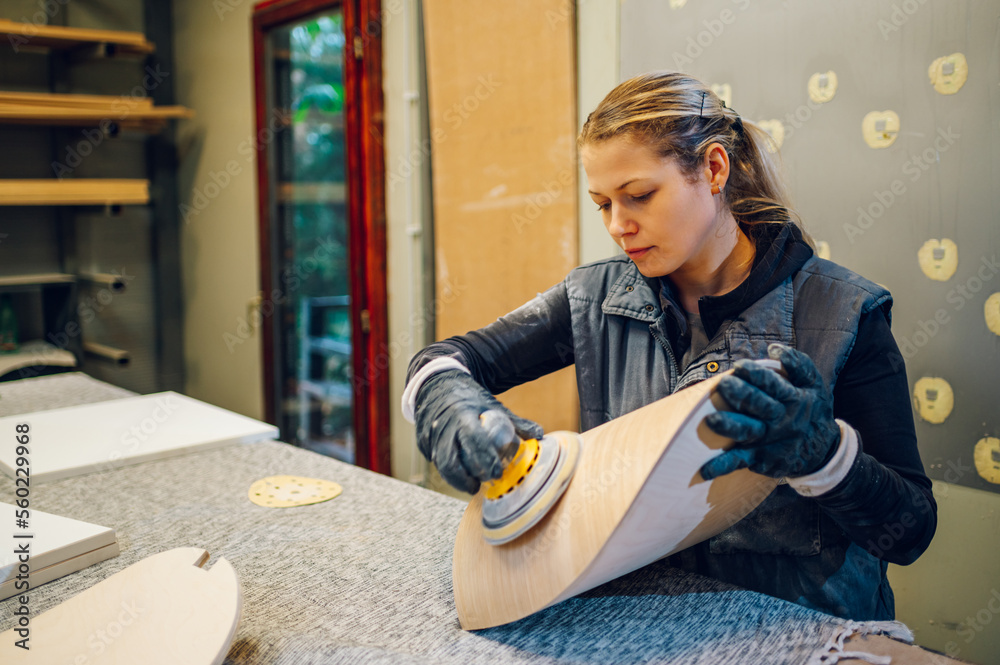 Blonde female carpenter using an electric sander in a workshop or factory Blonde female carpenter using an electric sander in a workshop or factory