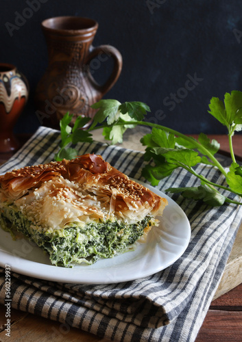 Cucina greca tradizionale. Spanakopita, un pezzo di torta di pasta fillo greca con ripieno di formaggio feta e spinaci su piatto bianco.